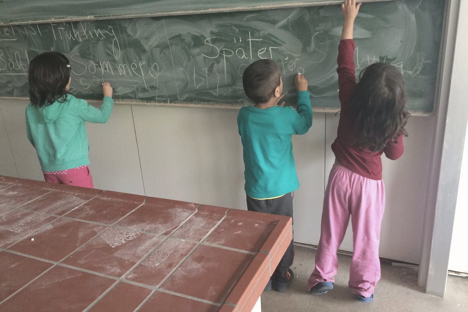 Drei Kinder schreiben an einer Schultafel